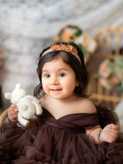 A close-up portrait of a beautiful baby girl holding her teddy bear. Sitter sessions are perfect for capturing those chubby cheeks and curious eyes.