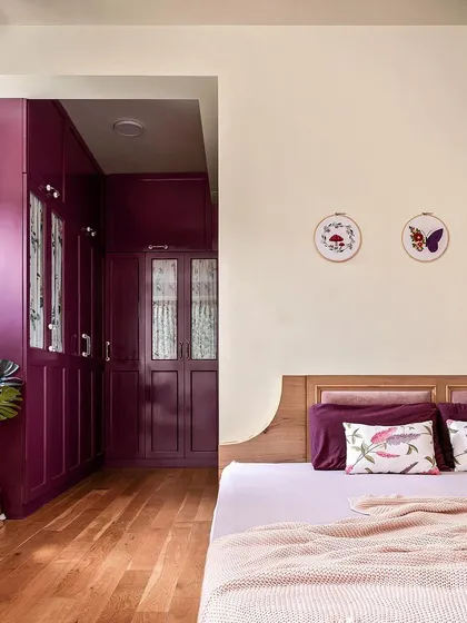 Another view of the eclectic guest bedroom, showing the full effect of the bold wine-colored wardrobes. The rich color creates a cozy and dramatic atmosphere in the space.