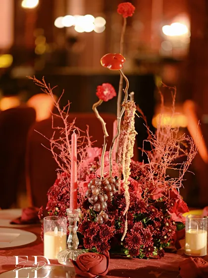 The full centerpiece, a dramatic and textural arrangement of red flowers, dried branches, and fruits. The design is bold, artistic, and perfectly suited for an evening reception.