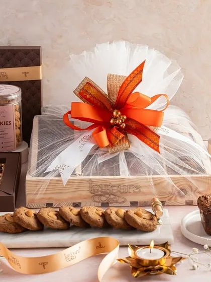 A cozy and indulgent Diwali hamper featuring a loaf cake, a wrapped gift crate, cookie jars, and boxes of brownies. This collection is perfect for a family to share and enjoy during the holiday.