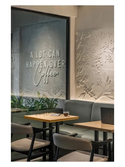 This view shows the layering of brand storytelling elements. The tagline on the glass is reflected on the interior wall, while the textured coffee plant mural adds a deeper narrative layer.