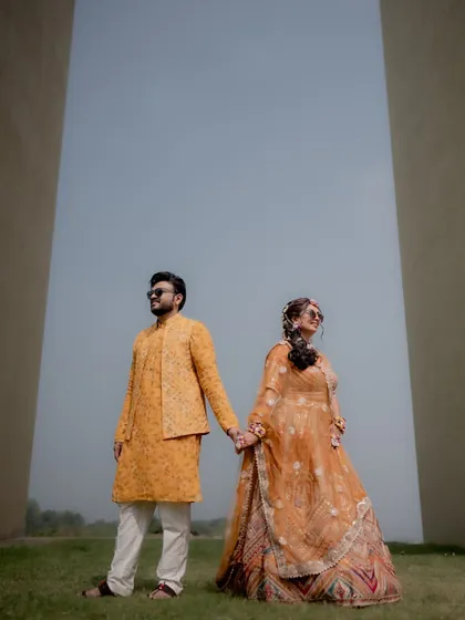 A stylish portrait of the couple holding hands after their Haldi ceremony, looking cool and happy in their matching yellow outfits.