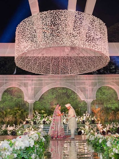 A full view of the couple during their ceremony, showcasing the scale and symmetry of the stage design. The all-white and green palette creates a serene and elegant atmosphere.