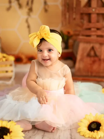 This sweet sitter session features our bright and cheerful sunflower theme. The setup includes a pastel rainbow dress and a backdrop of sunflowers, creating a beautiful portrait of a happy, smiling baby.