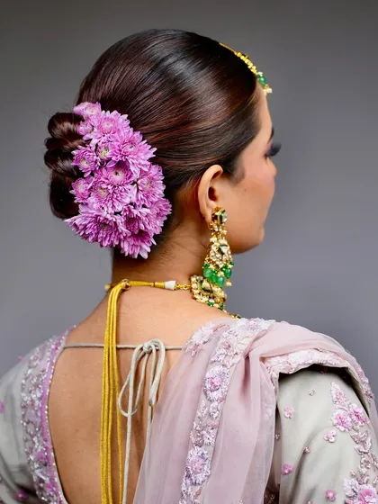 A classic for a reason. This elegant twisted bun, adorned with a cascade of fresh purple chrysanthemums, is a timeless choice for the main wedding day. It’s structured to hold the dupatta securely and stay perfect through all the ceremonies.