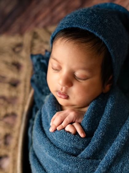 A close-up portrait focusing on the baby's peaceful face. The soft, fuzzy pom-pom on his hat adds a whimsical touch to this cozy wrapped pose.