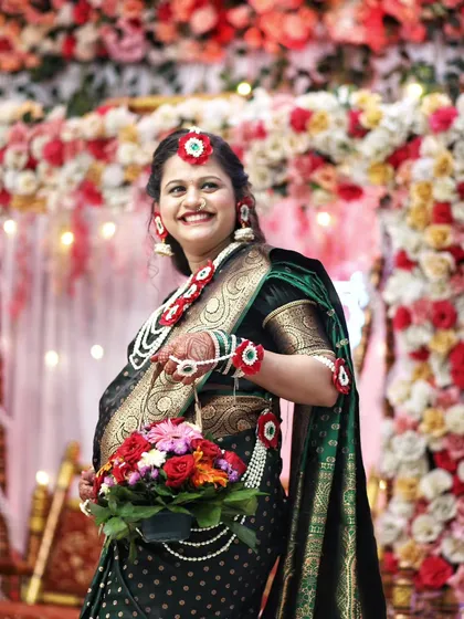 A radiant mother-to-be smiles brightly during her baby shower, holding a basket of fresh flowers. The vibrant floral decor in the background complements her traditional look.