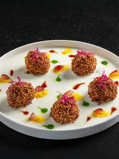 Dahi ke kebab presented elegantly on a bed of yogurt with colorful chutneys, creating a visually appealing starter.