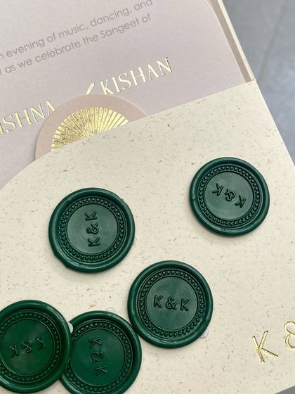A close-up of custom wax seals in a deep emerald green, stamped with the couple's 'K&K' monogram. The seals are placed next to the gold-foiled invitation, showing how different textures can work together.