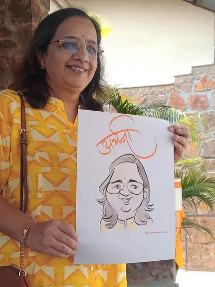 A woman proudly displays her caricature, which includes her name "Archana" in elegant Marathi script.