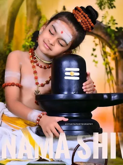 A child dressed as a Shiva devotee, hugging the Shiva Linga with eyes closed in devotion.