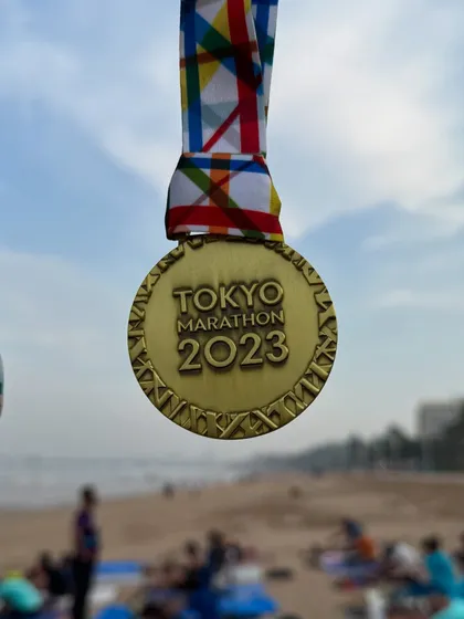 The 2023 Tokyo Marathon medal, held up against the backdrop of our Juhu beach training ground. We bring world-class goals to our local community.