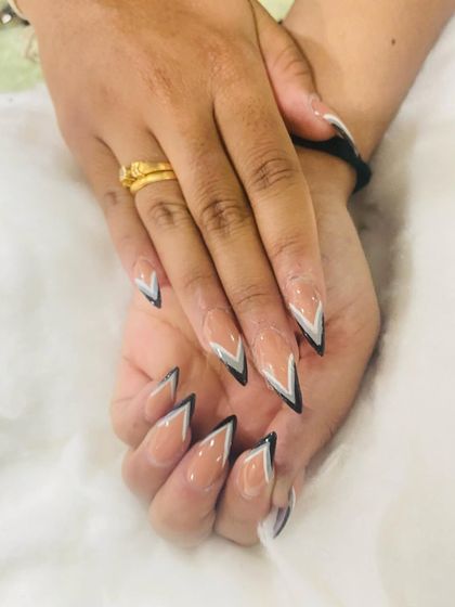 A very graphic and sharp V-shaped French tip in black, white, and silver. This geometric design on long stiletto nails is modern and makes a bold statement.