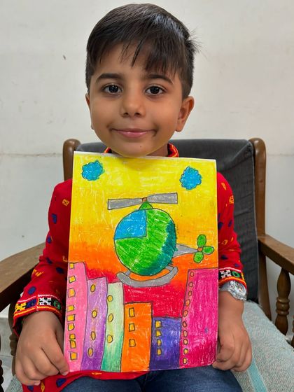 A 2nd-grade student proudly presents his drawing of a helicopter flying over a colourful city. We learn to draw different vehicles and create imaginative cityscapes.