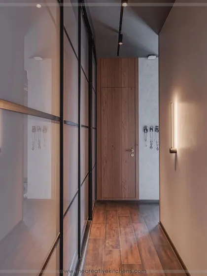 This angle shows how the back-painted glass wardrobe complements the warm wood flooring and door. The track lighting above highlights the wardrobe's impressive height and flawless finish.