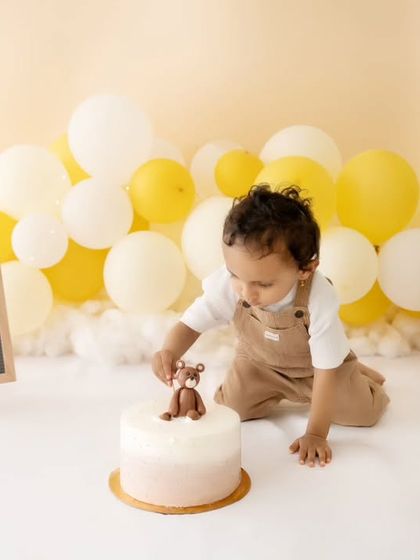 A curious little one reaching for the teddy bear topper on his birthday cake.