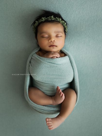A beautifully swaddled newborn in a classic "potato sack" pose, showing off their tiny toes. The simple green wrap and matching headband create a cohesive, natural look.