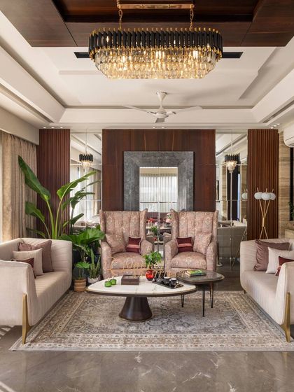 This living room design uses wall mirrors and a large chandelier to create a sense of grandeur and space. The warm wooden interiors and lush plants add a natural, refreshing touch.