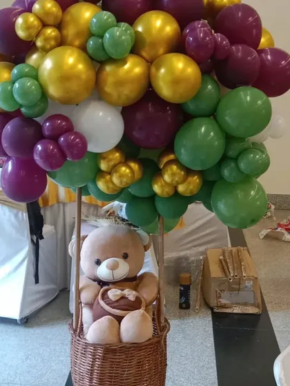 A creative hot air balloon centerpiece made with a wicker basket, a teddy bear, and a large bunch of colorful balloons on top. This is a great statement piece for a travel or adventure theme.