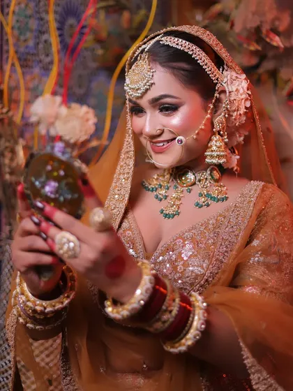 A candid moment as the bride looks into a mirror, her smile reflecting her joy. This is a classic Karwa Chauth themed shot.