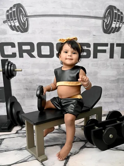 Getting her reps in early! This little girl is all business in her CrossFit-themed photoshoot, sitting on a miniature workout bench. It's a fun and strong theme for a baby girl.