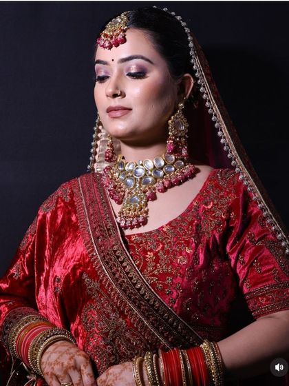 A close-up portrait of a bride in a red velvet lehenga, showcasing the detailed craftsmanship of the Polki and ruby choker set against the rich fabric.