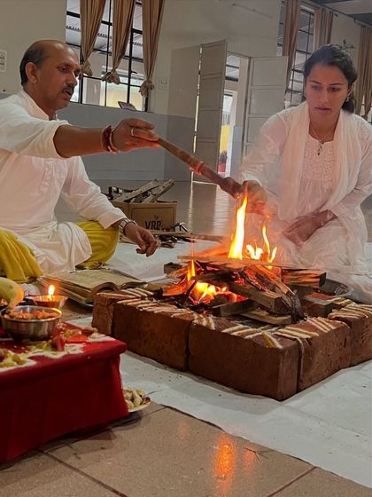 Two participants make offerings to the fire during a Ganapati Homam. This act of offering is a key part of karma yoga, performed with devotion and without expectation of personal gain.