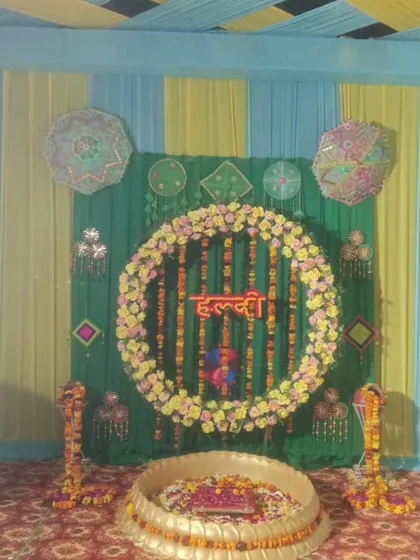 A traditional Haldi setup with a circular marigold backdrop and a large brass urli. The blue and yellow drapes in the background add a unique color combination.