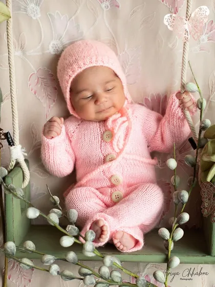 Swinging into sweetness in a cozy pink knit outfit. This delicate swing setup, adorned with pussy willows, is perfect for a soft and dreamy newborn portrait.