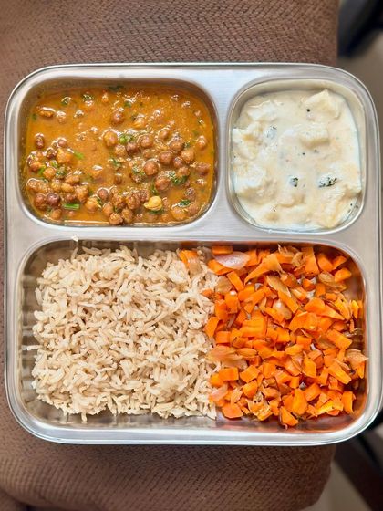 This plate features brown rice, black chickpea curry, sautéed carrots, and a potato raita.