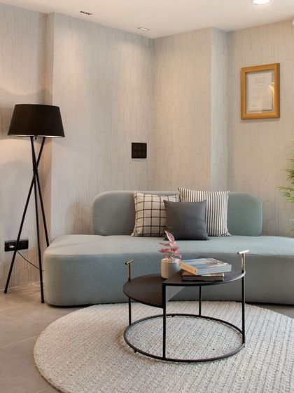 This sitting area in a modern office space elevates the art of the meeting. The curved sofa, tripod floor lamp, and textured rug create a sophisticated yet comfortable atmosphere for collaboration.
