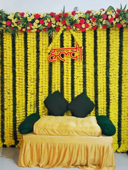 A simple and neat Haldi seating arrangement for a home ceremony, with a backdrop of yellow marigold strings and a comfortable yellow-covered sofa.