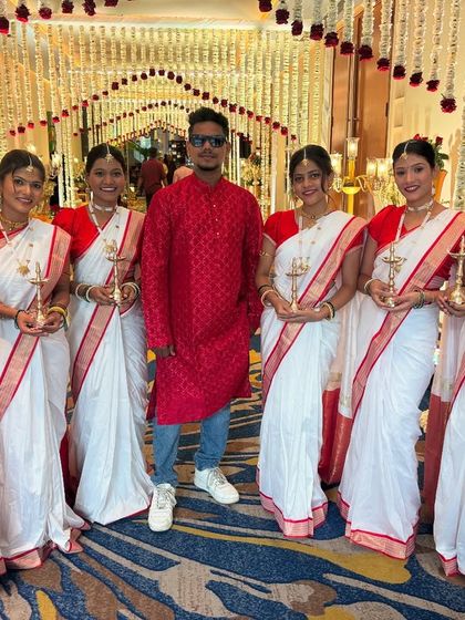 Our bridal entry team poses in the beautifully decorated hallway before the performance. Dressed in traditional white and red sarees and holding brass diyas, they are ready to create a serene and stunning entrance.