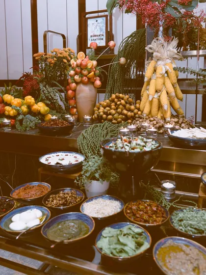 A wider view of a custom grazing table reveals the full story. Here, you can see the variety of serving dishes, from rustic bowls filled with dips and salads to a sculptural tower of corn, all arranged to create a landscape of abundance and artistry.
