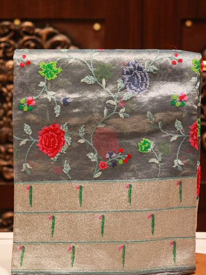 The full view of the grey tissue silk saree, showcasing the beautiful contrast between the subtle body and the colorful embroidery.