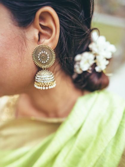 Beauty is in the details. This shot highlights a traditional gold jhumka earring and the delicate gajra of fresh flowers in the bride's hair, elements that define a classic Indian bridal aesthetic.