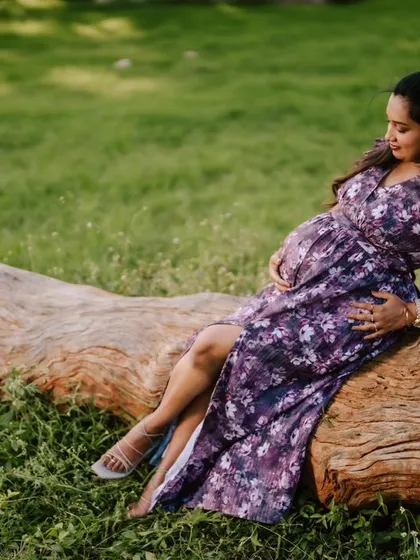A full-length view of the mom-to-be relaxing on a log, her floral dress complementing the natural surroundings perfectly.