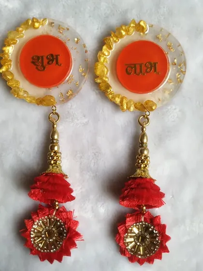This is another design for my 'Shubh Laabh' hangings. This version has a clear base with gold flakes and a central orange circle, paired with a bright red and gold tassel for a festive look.
