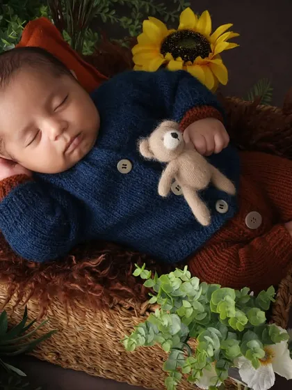Dreaming of cuddles. This peaceful pose, with the baby holding a tiny teddy, is the essence of newborn innocence. The surrounding greenery and sunflowers add a touch of nature's beauty.