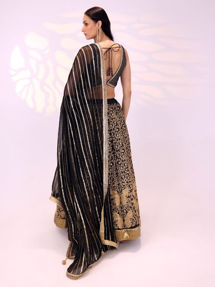 The back view of the black and gold lehenga is just as stunning, with a deep back and delicate ties on the blouse, and a full view of the striped dupatta.
