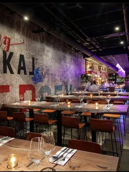 The interior of LokalJC, featuring rustic wooden tables and a large-scale wall graphic. The design blends industrial elements with a raw, artistic energy.