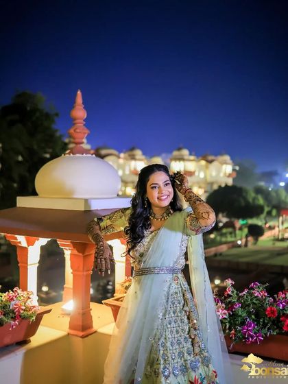A solo portrait of the bride during her engagement night, with the beautifully lit venue in the background. She looks radiant and happy.