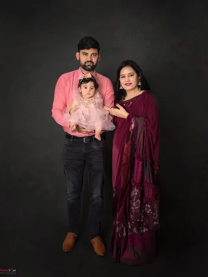A classic family portrait against a simple dark background. The coordinated outfits in shades of pink and maroon create a lovely, warm color palette.
