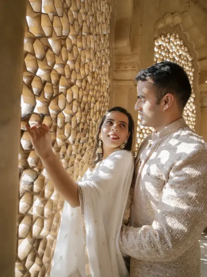 A candid moment of discovery by the intricate jali screens. The play of light and shadow adds a layer of artistry to this romantic couple photo, capturing their curiosity and connection.