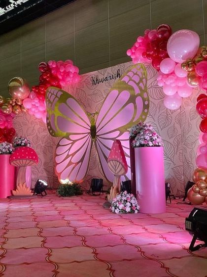 A beautiful butterfly-themed stage in shades of pink and red, featuring a large butterfly centerpiece, mushroom props, and floral arrangements.