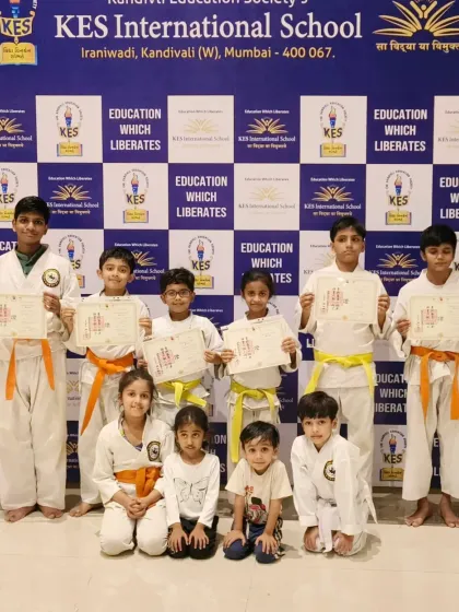 This photo captures a mix of beginner and intermediate students at KES International School. You can see the progression from younger children just starting to older students who have earned their orange belts.