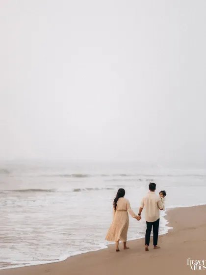 A family of three walks hand-in-hand along a misty shoreline. This wide shot creates a cinematic feel, emphasizing their journey together against the vastness of the ocean.