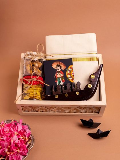 The complete 'Onasanchari' hamper, presented in a light wooden box. It features a kasavu mundu, a miniature Chundan Vallam, and jars of traditional snacks, offering a complete Onam experience.