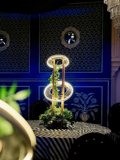 A close-up of the modern centerpiece, showing the detail of the illuminated rings and the greenery against the ornate blue wall.