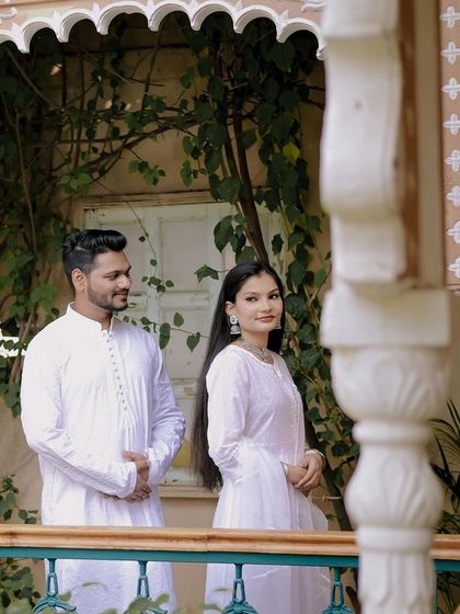 A classic portrait of the couple on a balcony. The groom looks on admiringly as the bride gazes at the camera, capturing a quiet and confident moment.